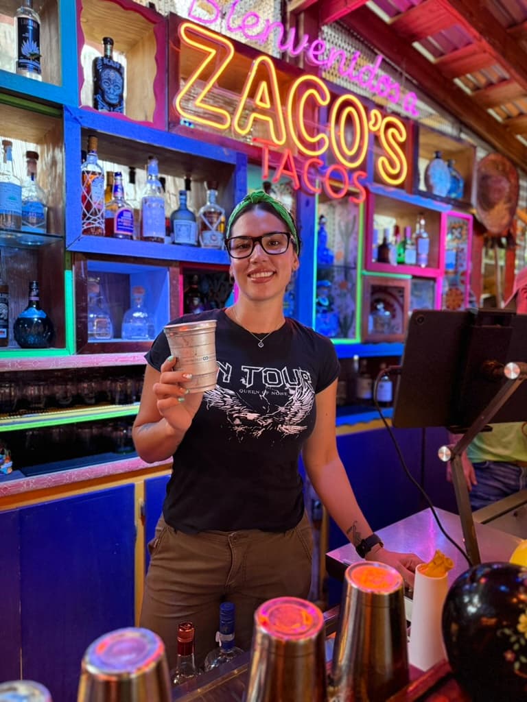 Bartender smiling in front of Bienvenidos neon sign